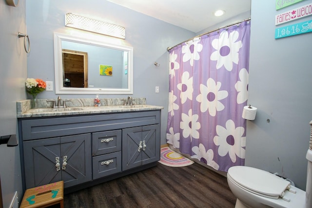 bathroom with double vanity, a sink, toilet, and wood finished floors