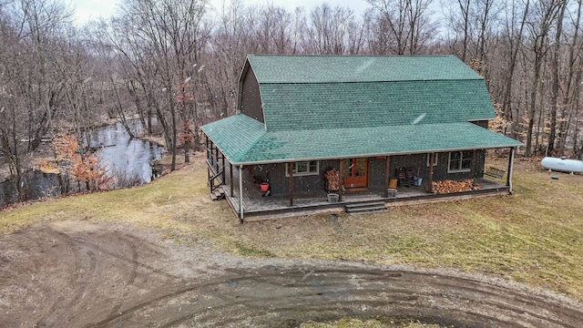 view of front of home with roof with shingles, a front lawn, a wooded view, and a gambrel roof