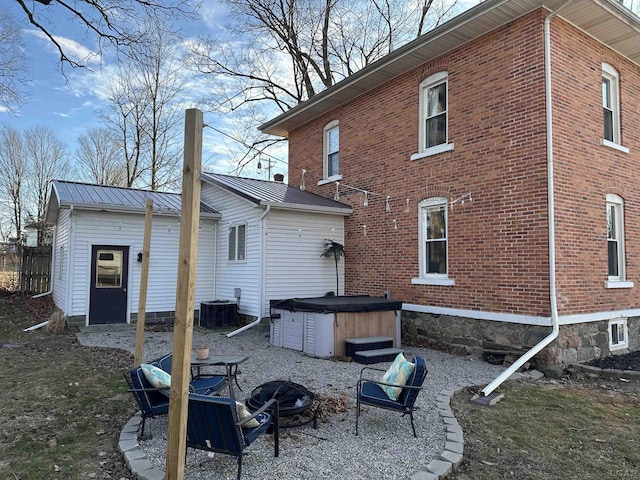 back of house featuring an outdoor fire pit, brick siding, metal roof, and a hot tub