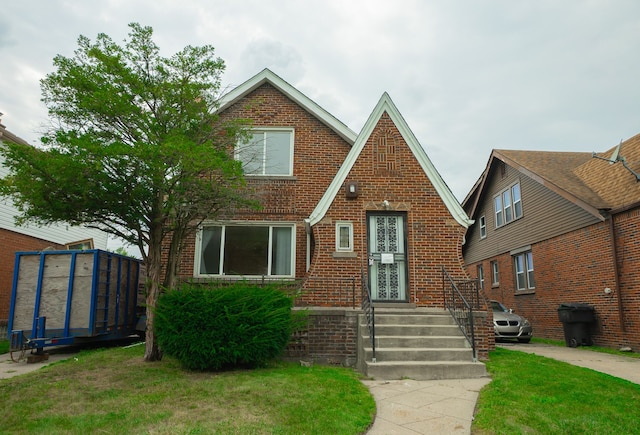 english style home with brick siding and a front yard