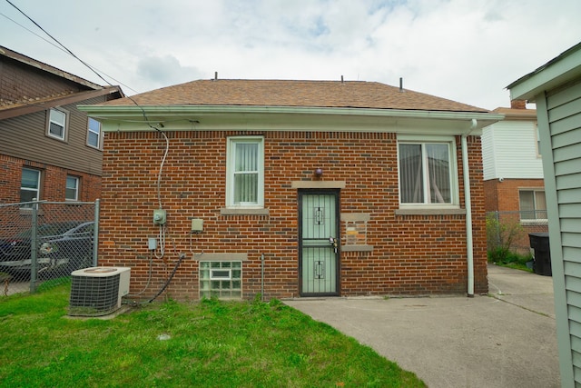 rear view of property featuring brick siding, a shingled roof, a lawn, central AC, and fence