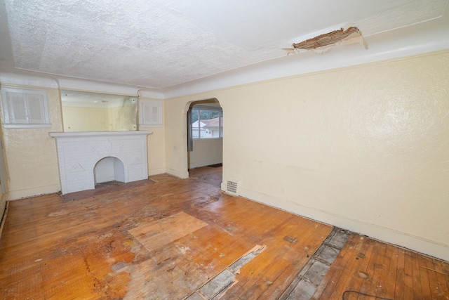 unfurnished living room with arched walkways, a textured ceiling, a fireplace, visible vents, and wood-type flooring