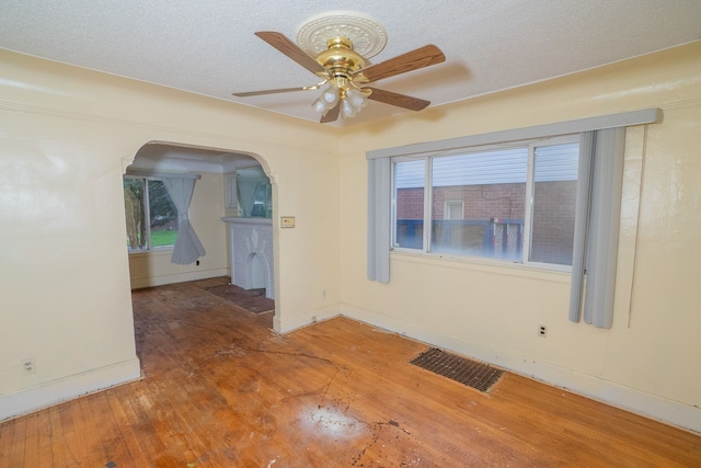 empty room featuring visible vents, hardwood / wood-style floors, a ceiling fan, a textured ceiling, and baseboards