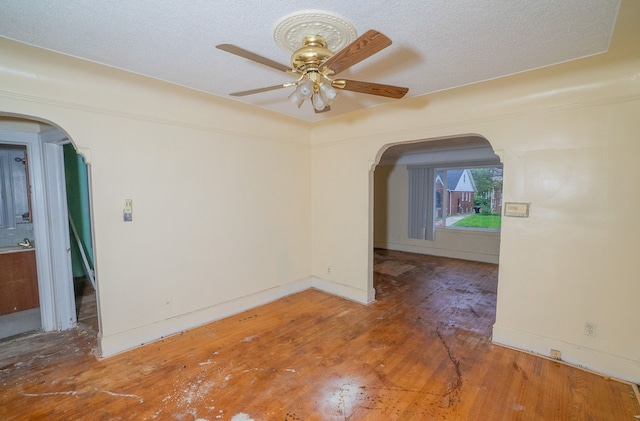 spare room with baseboards, arched walkways, a ceiling fan, wood finished floors, and a textured ceiling