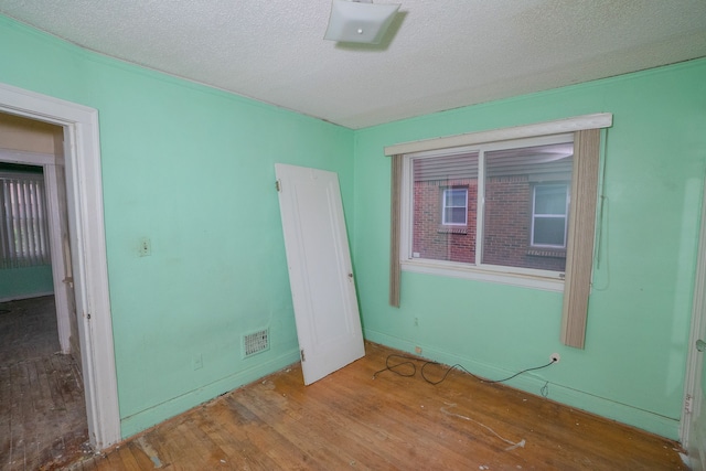 empty room featuring visible vents, a textured ceiling, and wood finished floors