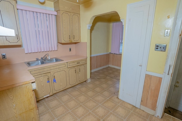 kitchen with arched walkways, a wainscoted wall, a sink, light countertops, and light floors