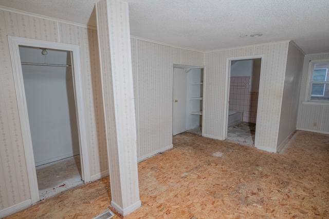 unfurnished bedroom with a textured ceiling, crown molding, baseboards, and wallpapered walls