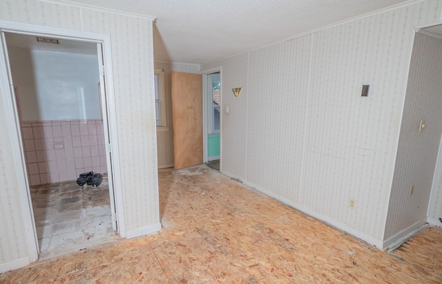 empty room with crown molding, a textured ceiling, wainscoting, and wallpapered walls