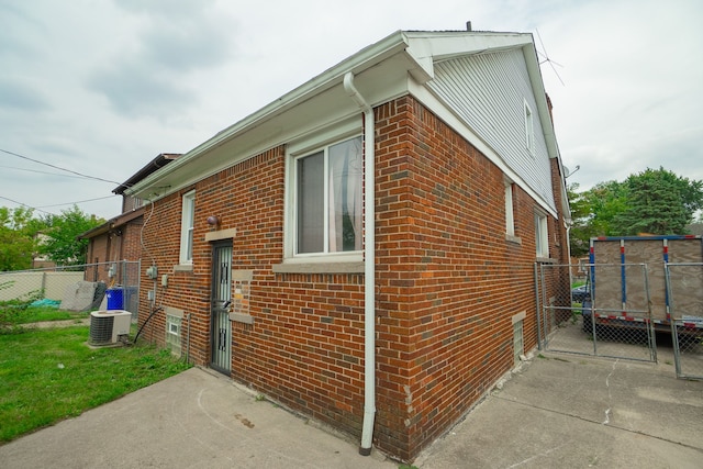 view of side of home featuring cooling unit, brick siding, and fence