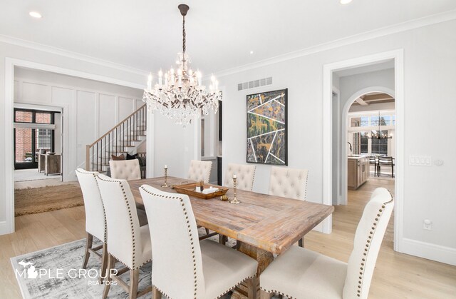 dining space with a chandelier, arched walkways, light wood-style flooring, visible vents, and ornamental molding