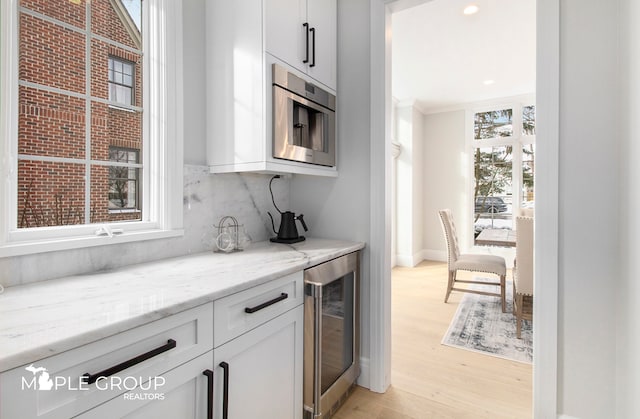 kitchen with wine cooler, light wood-style flooring, decorative backsplash, white cabinets, and light stone countertops