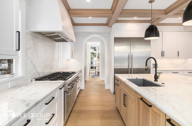 kitchen with light wood finished floors, high end appliances, a sink, coffered ceiling, and premium range hood