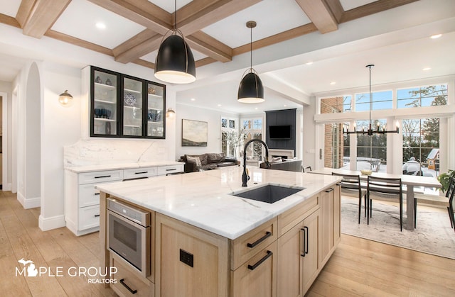 kitchen with glass insert cabinets, a sink, backsplash, and light wood finished floors