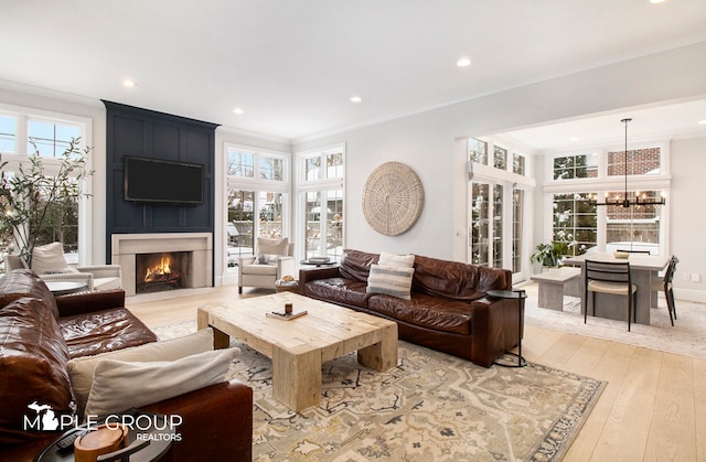 living area featuring a notable chandelier, a large fireplace, recessed lighting, light wood finished floors, and crown molding