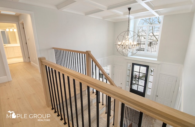 hall featuring beam ceiling, light wood-style flooring, an upstairs landing, a chandelier, and coffered ceiling