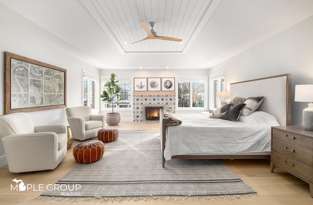 bedroom with a raised ceiling, wooden ceiling, a fireplace, and wood finished floors