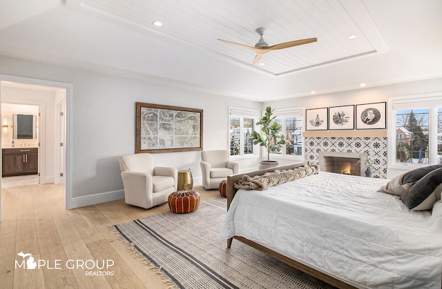 bedroom with a tray ceiling, multiple windows, a fireplace, and light wood-style flooring