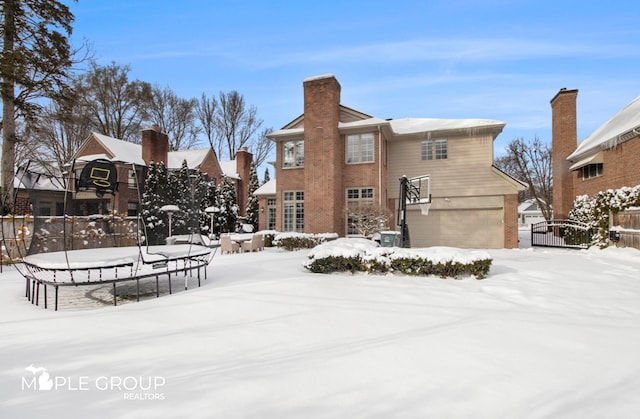 snow covered back of property featuring brick siding, an attached garage, and fence