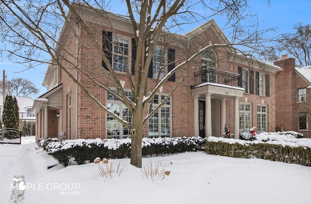 view of snow covered exterior with a balcony and brick siding