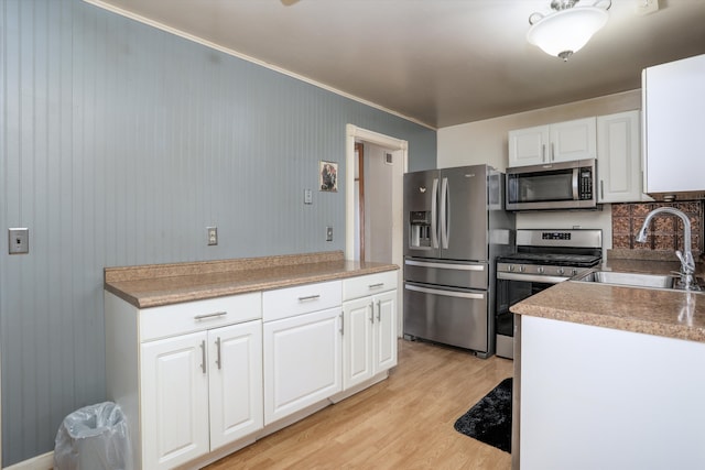 kitchen with light wood finished floors, stainless steel appliances, tasteful backsplash, white cabinets, and a sink