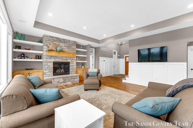 living room with a stone fireplace, recessed lighting, a wainscoted wall, wood finished floors, and visible vents