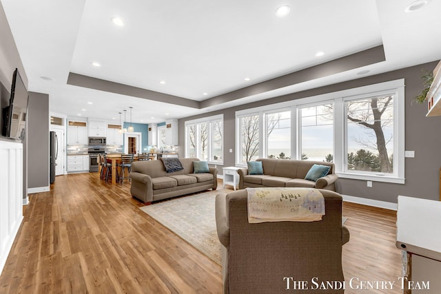 living area with light wood-style floors, baseboards, a tray ceiling, and recessed lighting