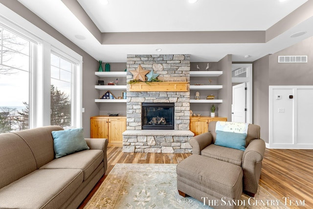 living area with a fireplace, visible vents, a raised ceiling, and wood finished floors