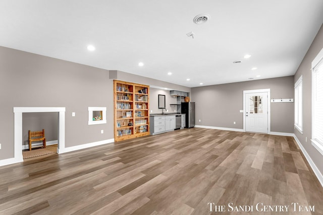 unfurnished living room featuring recessed lighting, a sink, visible vents, baseboards, and light wood-style floors