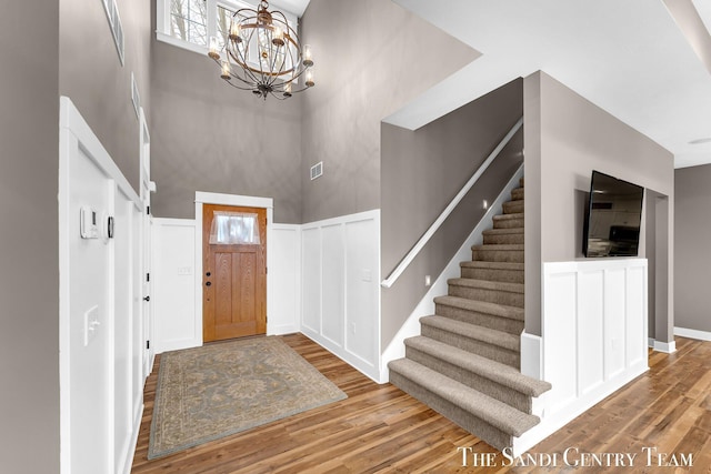 foyer entrance featuring a towering ceiling, stairway, wood finished floors, and wainscoting