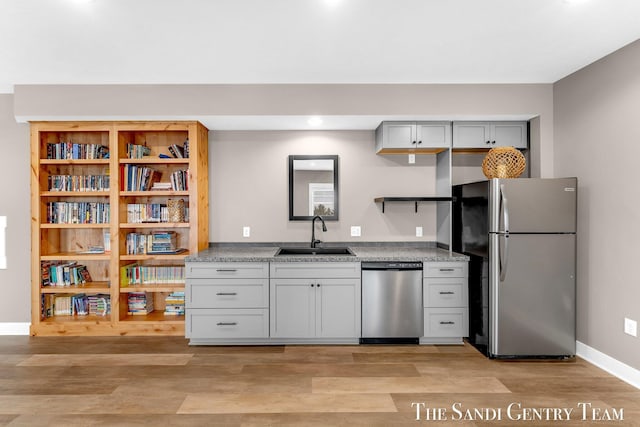 kitchen with stainless steel appliances, open shelves, light wood-type flooring, and a sink