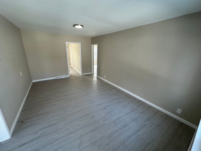 spare room with dark wood-style flooring, visible vents, and baseboards