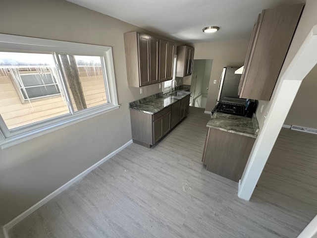 kitchen featuring a sink, visible vents, range with gas stovetop, baseboards, and light wood finished floors