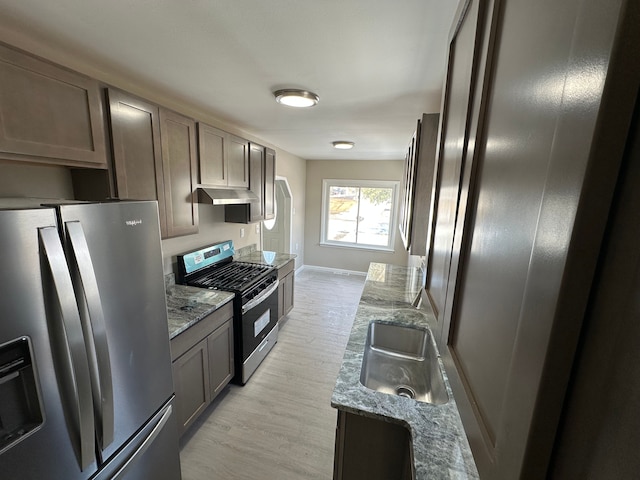 kitchen with light wood-style flooring, under cabinet range hood, a sink, appliances with stainless steel finishes, and light stone countertops