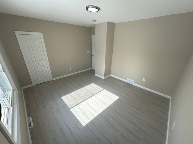 unfurnished bedroom featuring a closet, wood finished floors, visible vents, and baseboards