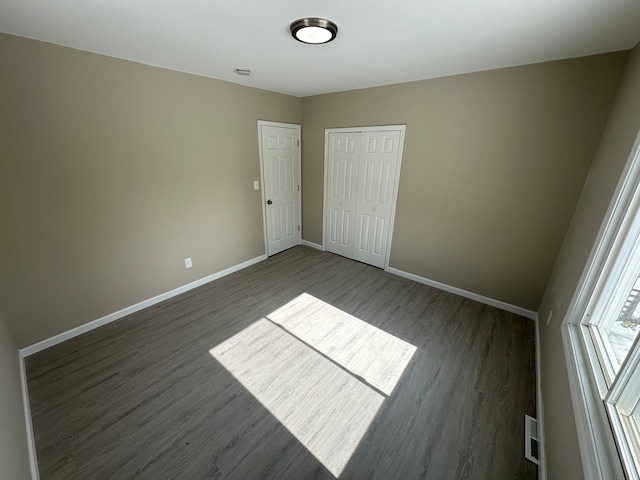 unfurnished bedroom featuring dark wood-style flooring, a closet, visible vents, and baseboards