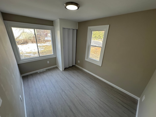 unfurnished bedroom with a closet, wood finished floors, visible vents, and baseboards