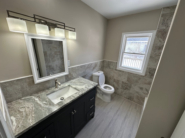 bathroom with a wainscoted wall, tile walls, toilet, and vanity