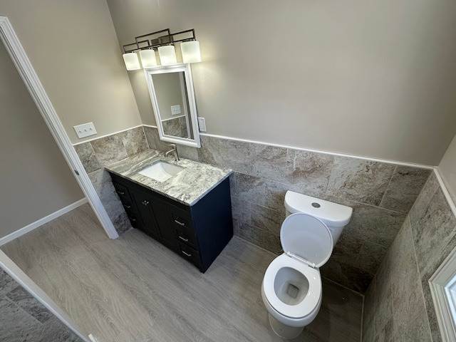 bathroom with toilet, wood finished floors, vanity, tile walls, and wainscoting