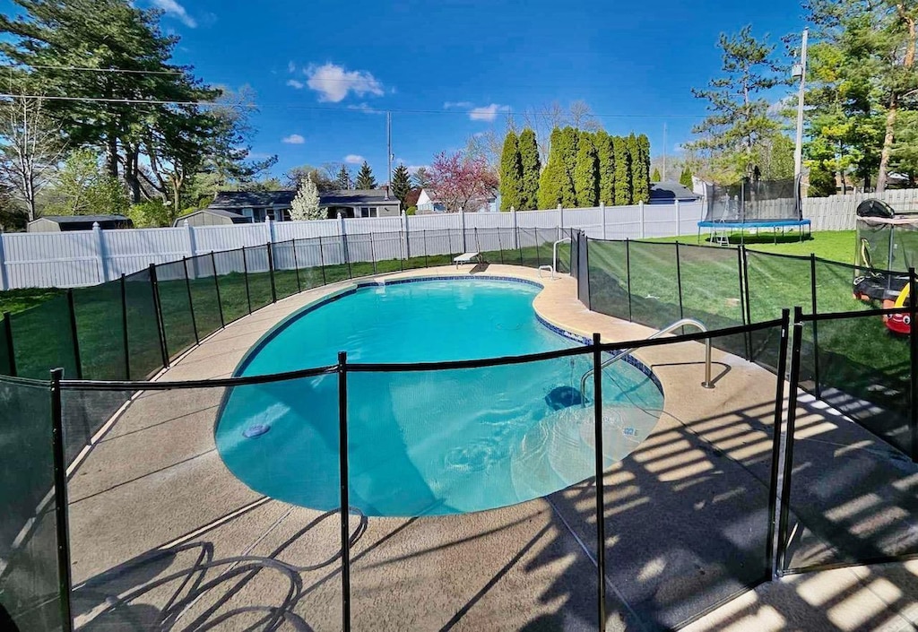 view of swimming pool featuring a trampoline, a fenced in pool, a patio, a lawn, and a fenced backyard