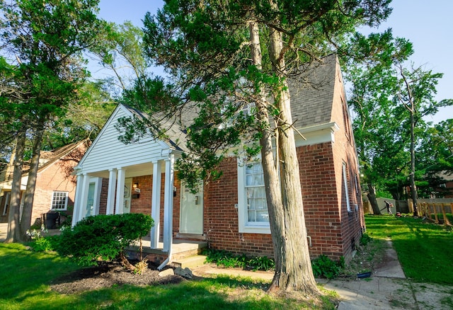 view of front facade with brick siding, a front lawn, and a shingled roof