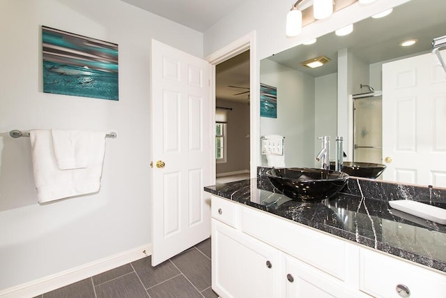 bathroom featuring double vanity, a sink, a shower with shower door, and baseboards