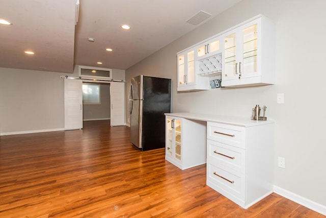 kitchen featuring glass insert cabinets, light countertops, wood finished floors, and freestanding refrigerator