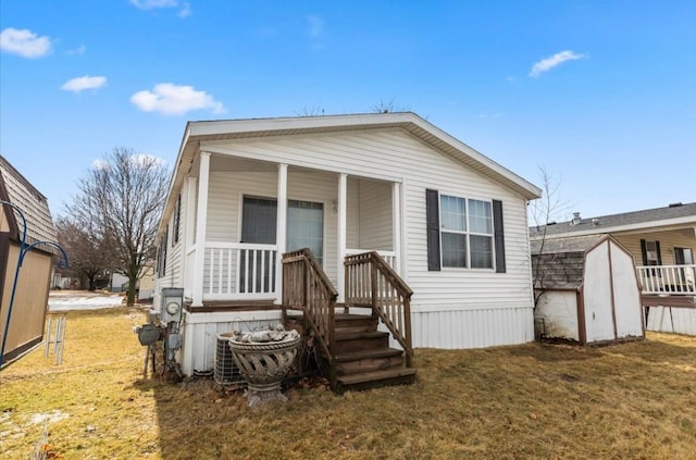 view of front of home featuring covered porch, a shed, a front yard, and an outdoor structure