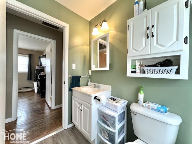 half bathroom with toilet, baseboards, wood finished floors, and vanity