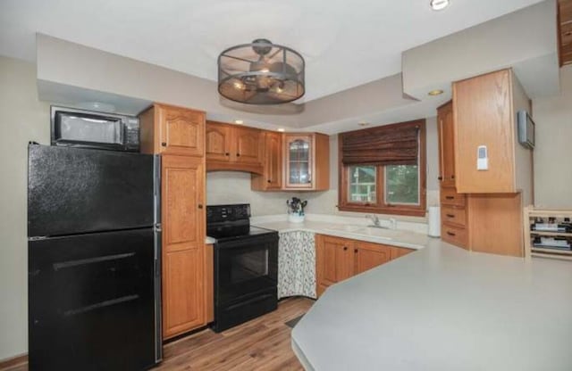 kitchen with a sink, light countertops, black appliances, light wood finished floors, and glass insert cabinets