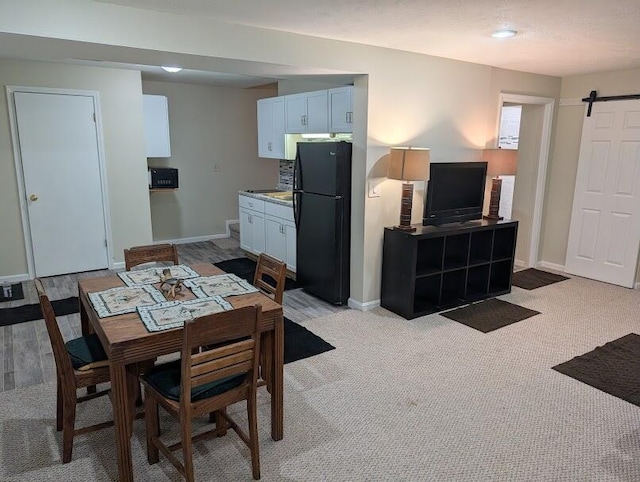 dining space featuring light carpet, a barn door, and baseboards