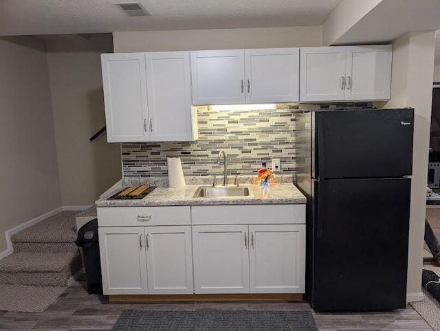 kitchen featuring visible vents, white cabinets, freestanding refrigerator, a sink, and backsplash