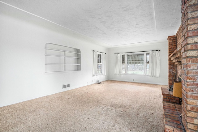 unfurnished living room with a textured ceiling, built in shelves, visible vents, baseboards, and carpet