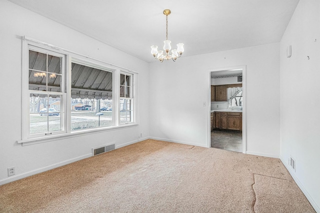 carpeted spare room with visible vents, baseboards, and an inviting chandelier