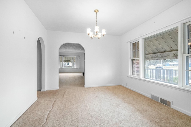 carpeted empty room featuring arched walkways, baseboards, visible vents, and an inviting chandelier